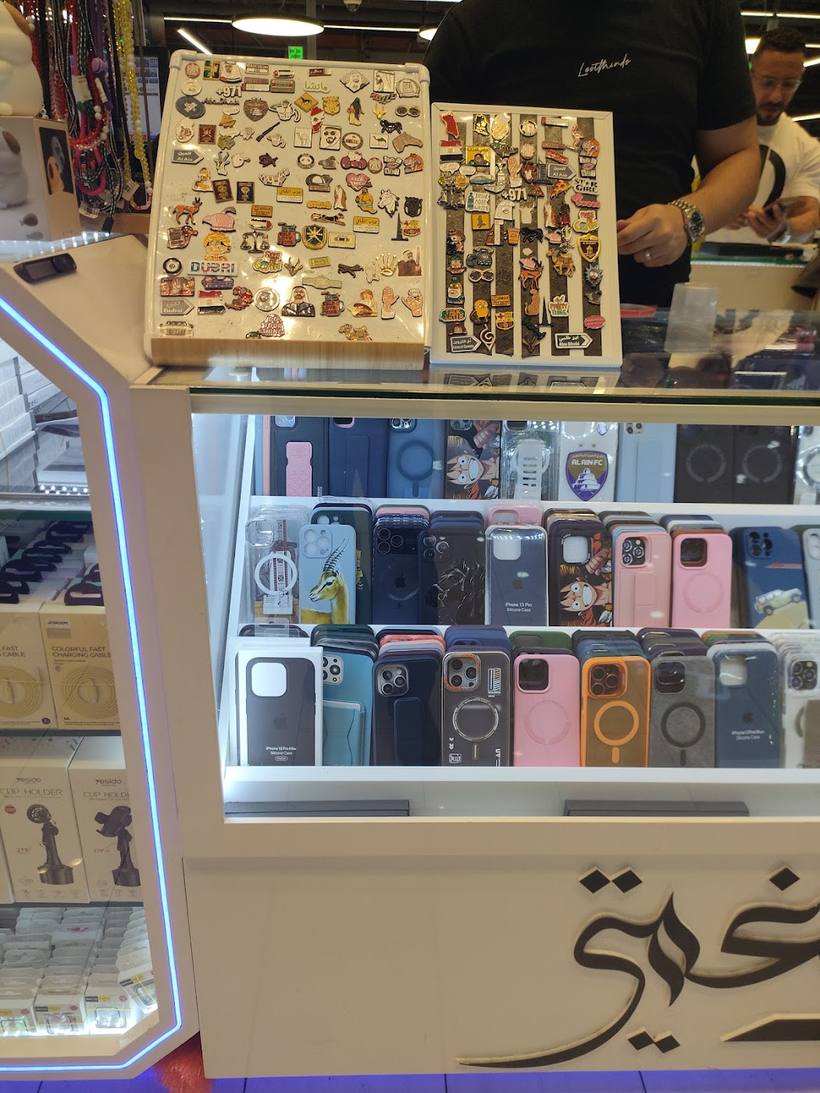 Trays of charms and keychains above a shelf of phone cases, with the Arabic نغمتي logo